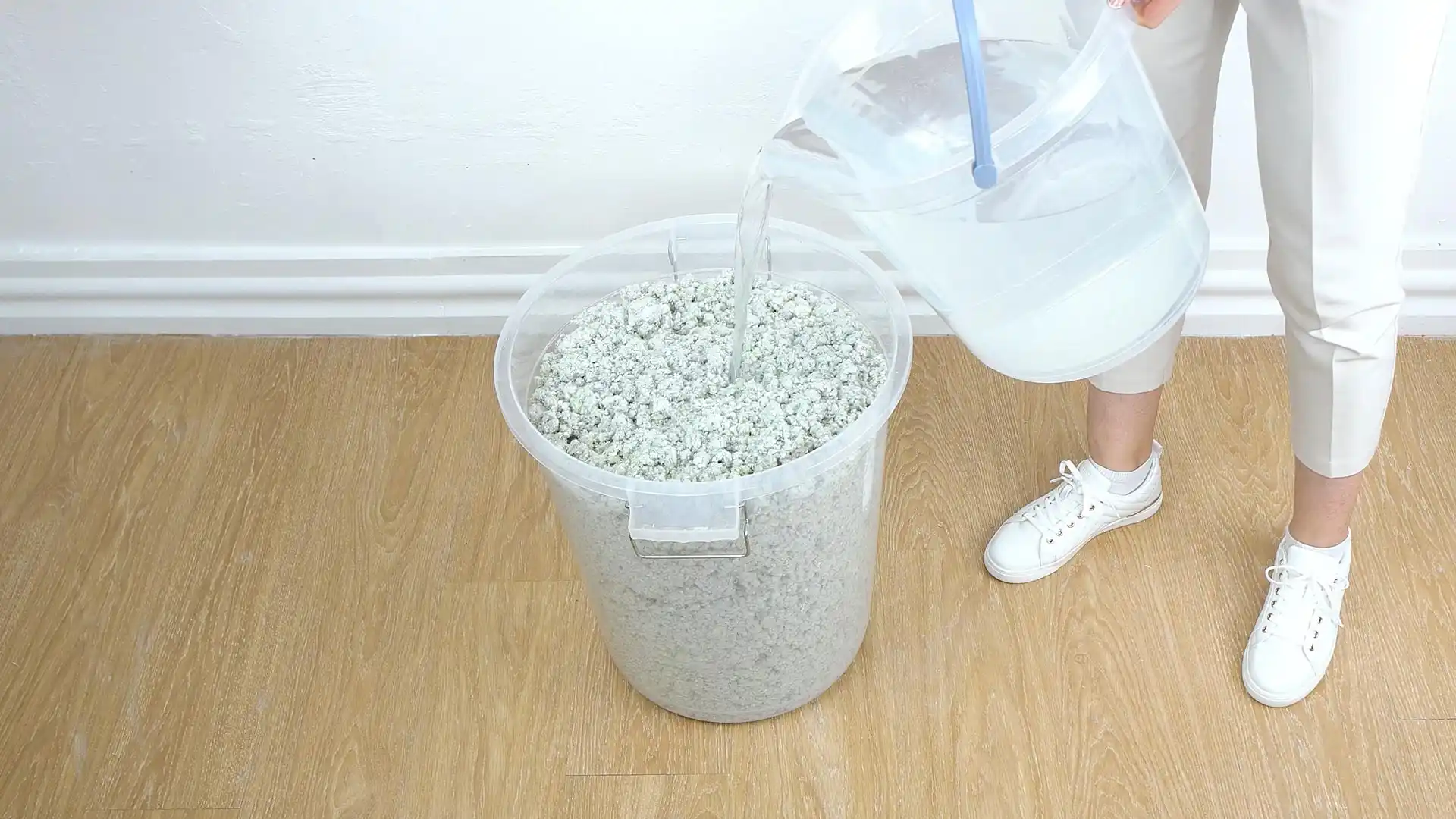 Handwarmes Wasser wird aus einem Messbecher direkt auf das trockene Belka Pulver im Eimer gegossen. Das Wasser dringt in die Fasern ein.